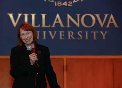 Dr. Patricia Grady stands with a microphone in front of a Villanova University sign.