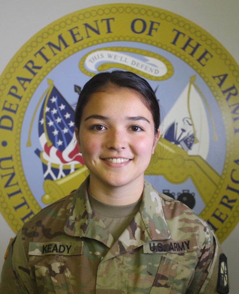 Katherine Keady, in her U.S. Army uniform, poses before the Department of the Army logo.
