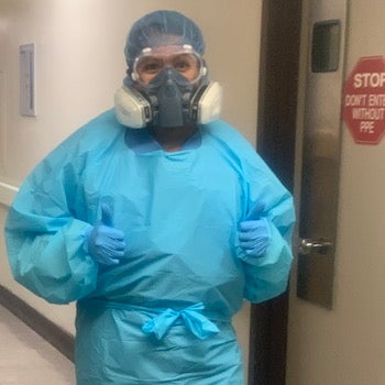 Jen Tran (NHS’11) in her personal protective equipment standing near a door that say Stop Don't Enter without PPE.