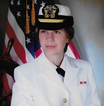 Carrie Bronson in her Navy uniform in front of the flag of the United States of America.