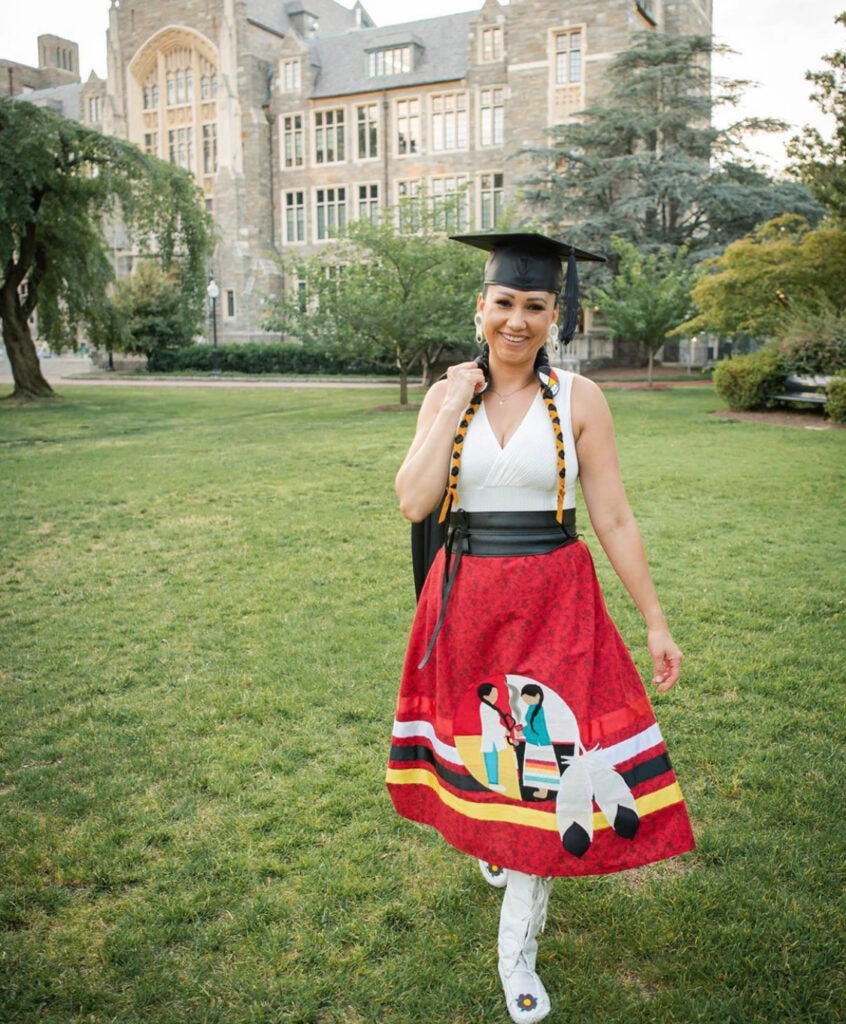 Nordica Owens stands in front of White-Gravenor Hall on Georgetown's campus wearing her graduation cap and a special ribbon skirt she had made to help connect "western medicine with traditional medicine."