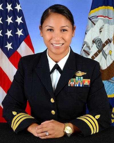 Commander Hannah C. Starnes (NHS’05) in her naval uniform in front of the United States flag and the United States Navy flag