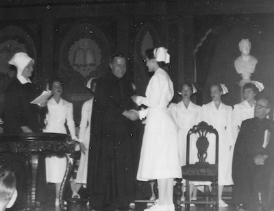 Nursing students on stage at a ceremony in Gaston Hall with priests and a sister