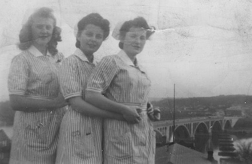In November 1942, three nursing classmates, in uniform, pose together, likely on the rooftop of the old hospital complex, with the Key Bridge behind them. 