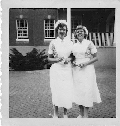 Two students, in the mid-1950s, stand in their nursing uniforms near Old North on Georgetown's campus.