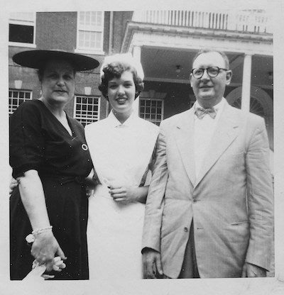A nursing student, in the mid-1950s, stands with her parents near Old North on Georgetown's campus in her nursing uniform
