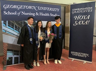 A group photo at Georgetown's Commencement at Nationals Park with individuals in academic gowns in front of a picture and sign that reads Georgetown University School of Nursing & Health Studies