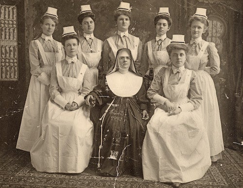 An image of a graduating class of nurses from Georgetown in the early 20th century wearing their nursing uniforms and posing with a religious sister who led the school.