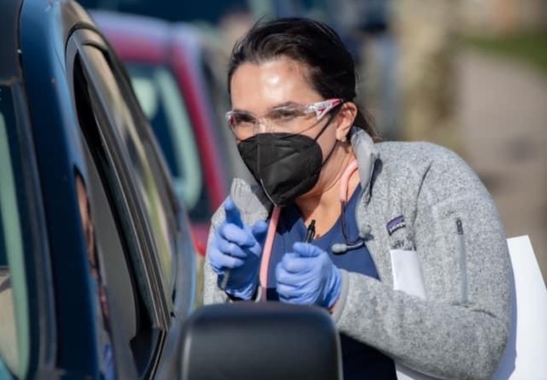 Dr. Melody Wilkinson, in gloves and mask, provides information to a driver in a car.