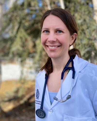 Cassie Bronson in her white clinical laboratory coat pictured in an outdoor setting in front of trees.