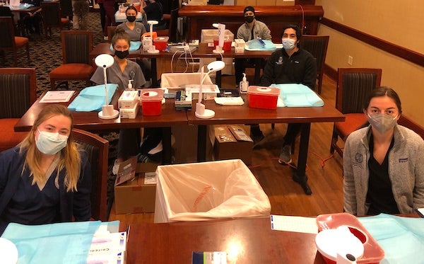 BSN and medical students sit at multiple tables, which are their vaccine stations
