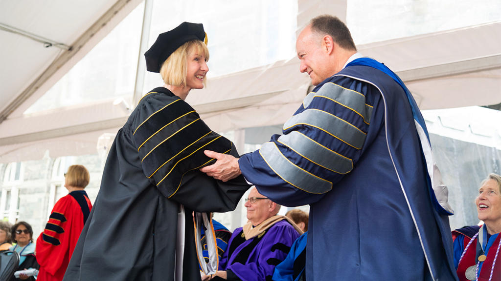 A PhD student at graduation in regalia shakes hands with President Jack DeGioia