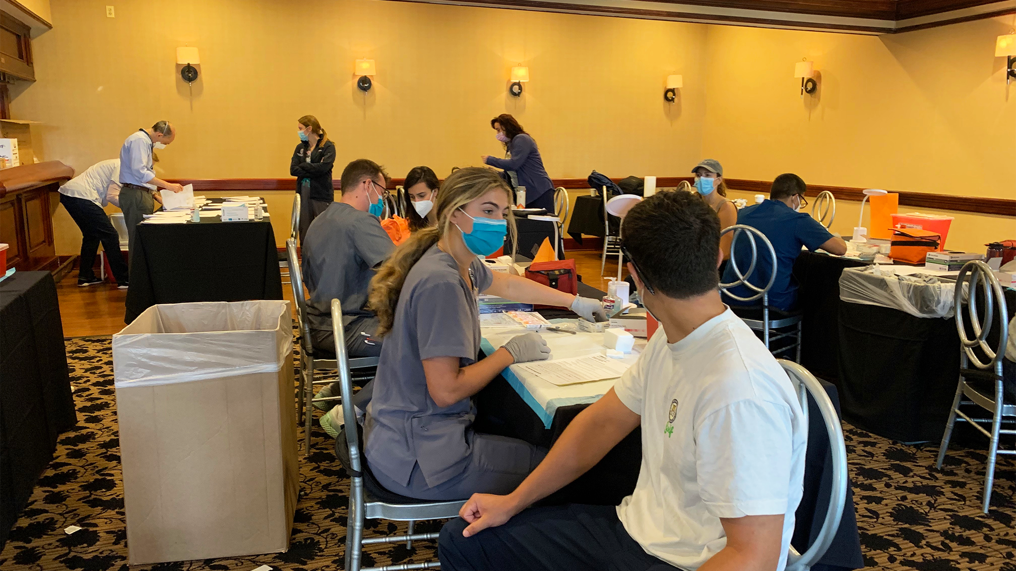 student medical personnel sit at tables and administer vaccines to other students