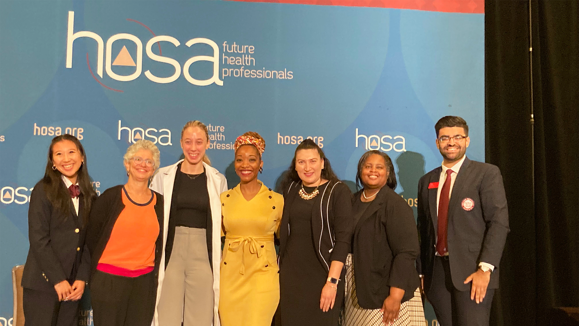 A group of people stand in front of a backdrop that reads HOSA