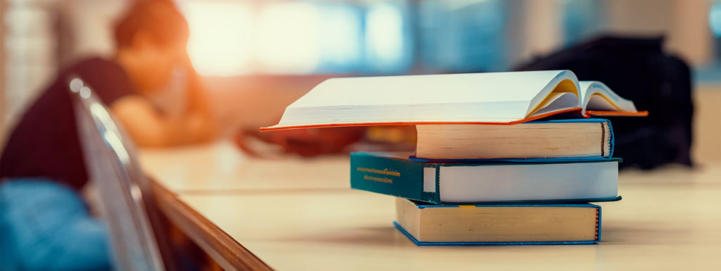 Library books in the foreground on a table with a person sitting in the background