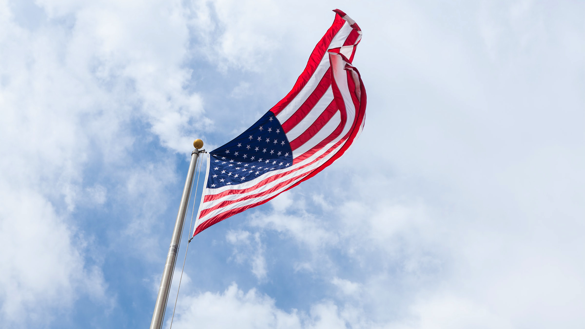 An American flag flies from a flagpole against a blue sky
