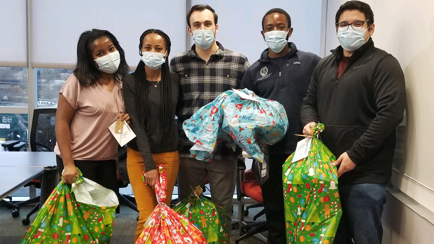 A group of students hold festive holiday bags filled with donated toys
