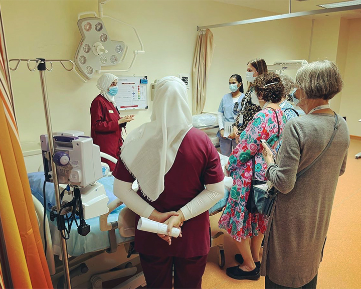 A group of visiting nurse midwives gather around a hospital bed to talk with nurses at a hospital in the UAE