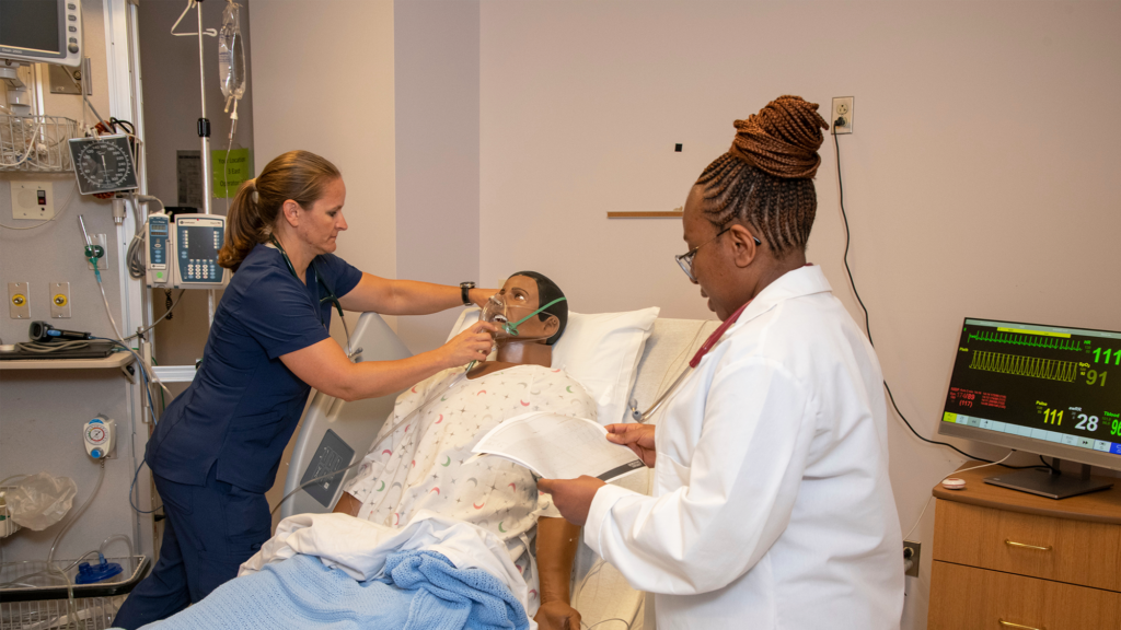 A nurse adjusts the oxygen mask on a simulator dummy while an instructor examines an EKG printout