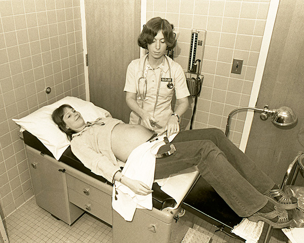 A nurse midwife examines a pregnant woman lying on an exam table