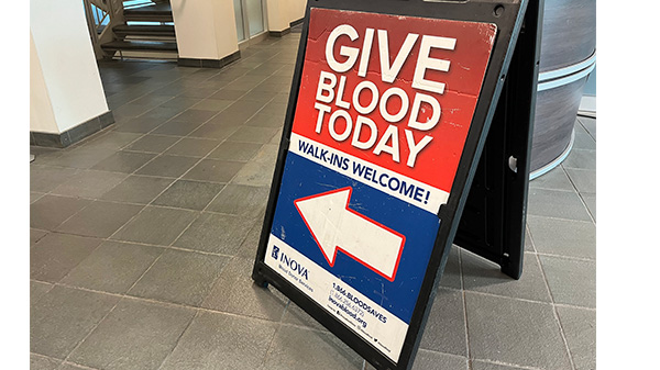 A sign reads Give Blood Today with a large white directional arrow