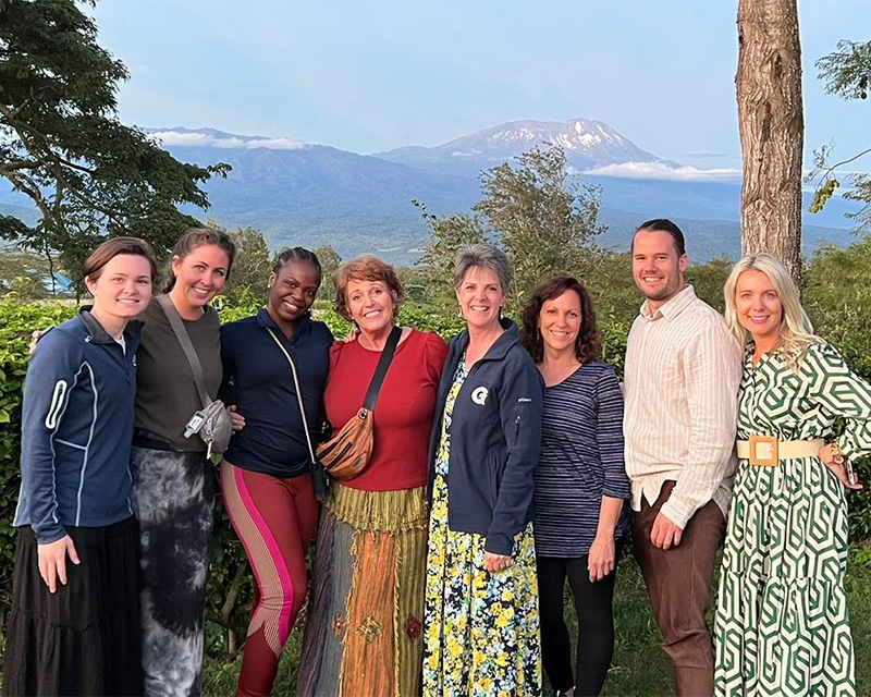 Eight individuals stand together with Mount Kilimanjaro in the background