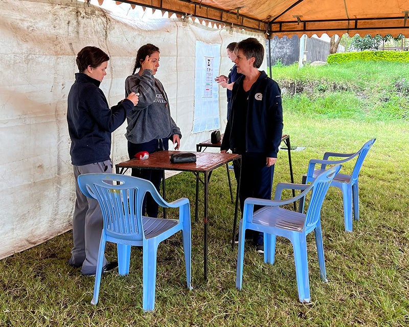 Four individuals stand in a tent readying equipment and tables and chairs