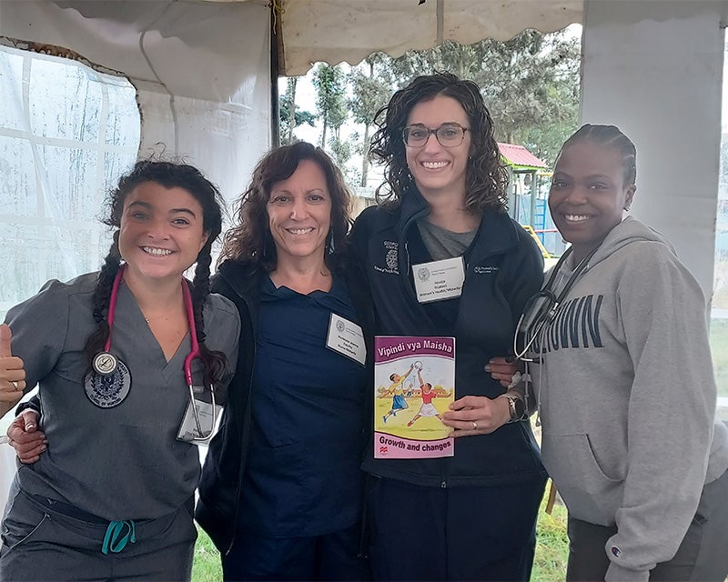 Three students and faculty member stand together, one holding a book called Growth and Changes