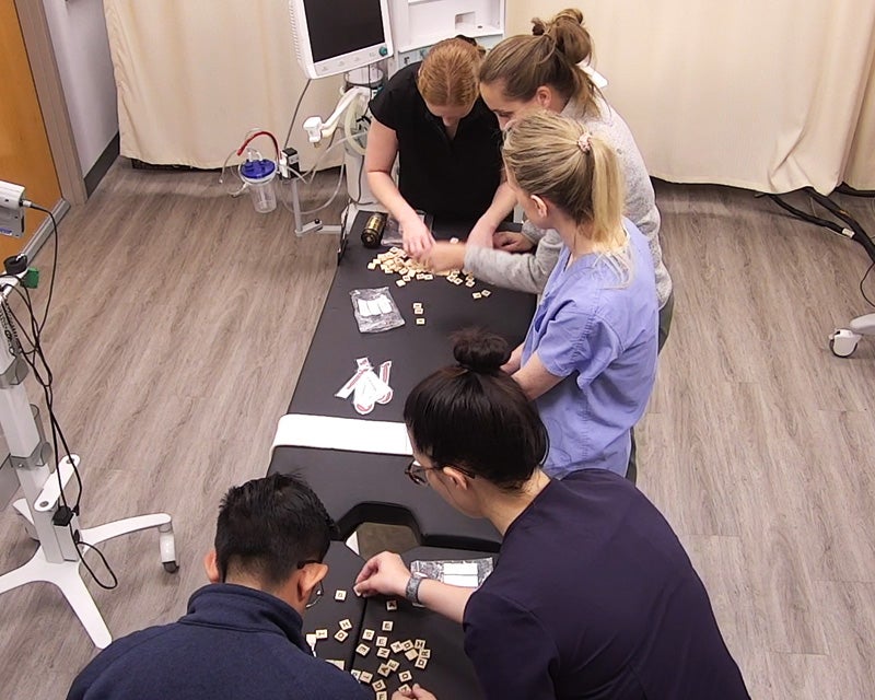 Five students work on puzzles in the SIM Center escape room scenario