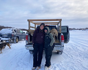 Wagner and another person stand side by side in front of a pickup truck with several dogs in the Alaska winter