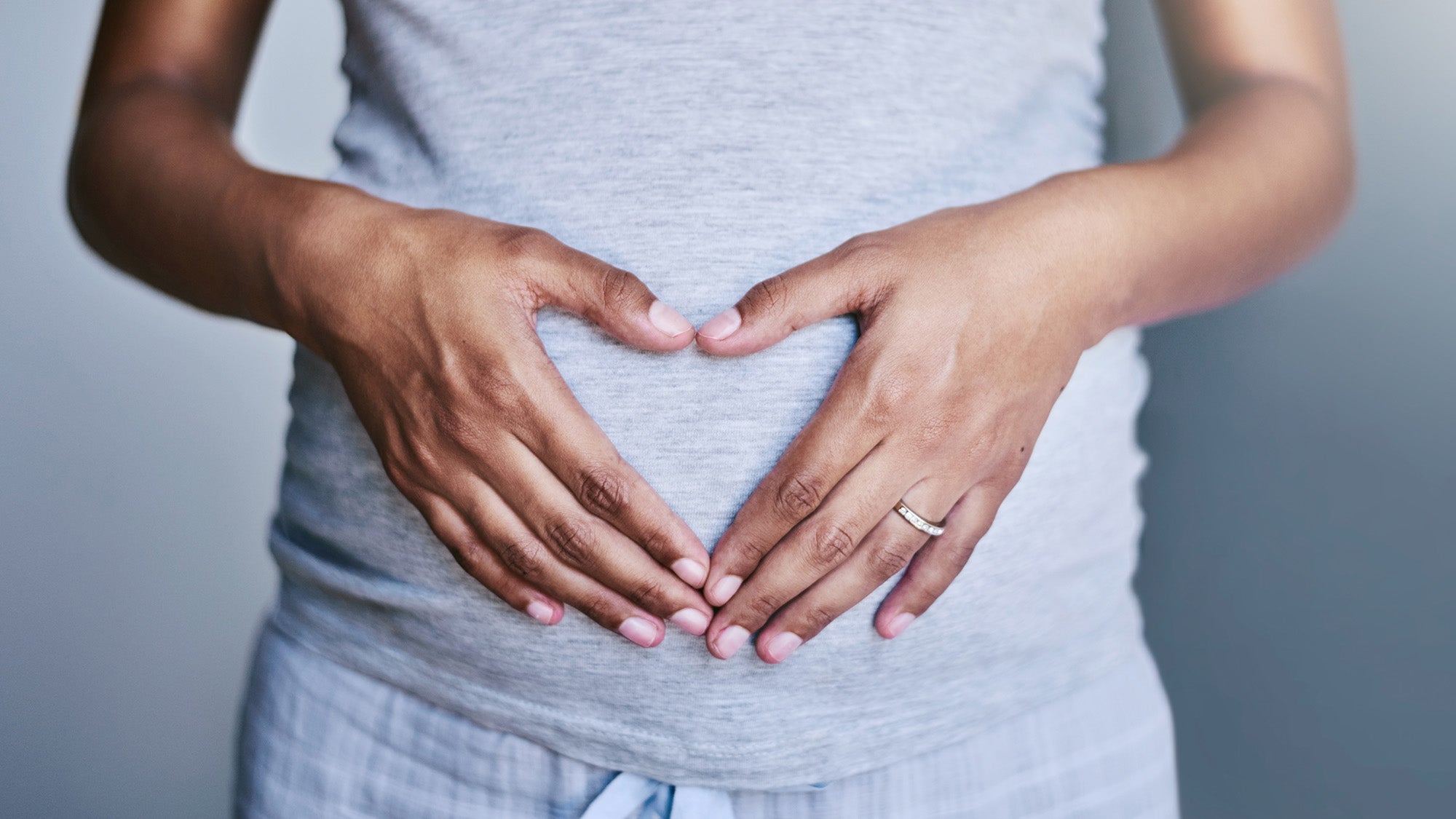 A pregnant person holds hands over their belly in the shape of a heart