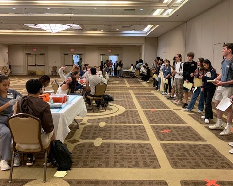 Students line the wall of the room waiting for nursing students to administer flu vaccines at tables before them