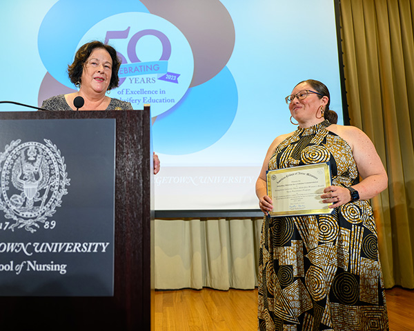 A woman stands behind a podium while another stands next to her holding a certificate