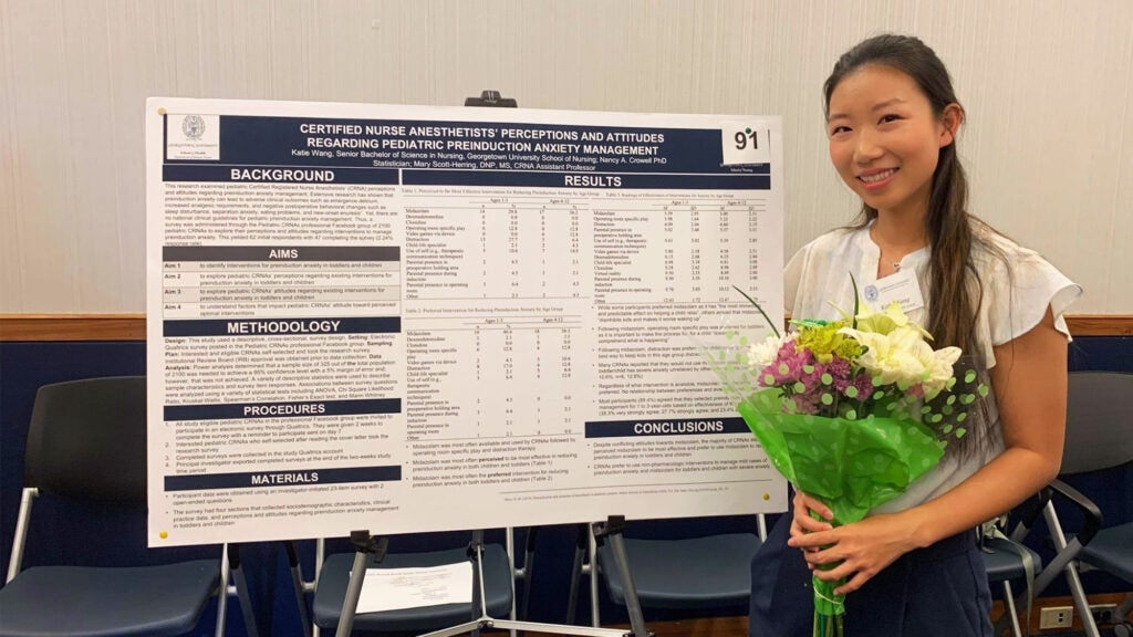 Katie Wang stands in front of her research poster holding a bouquet of flowers