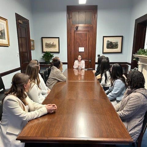 Students sit on either side of a long table in a congressional office