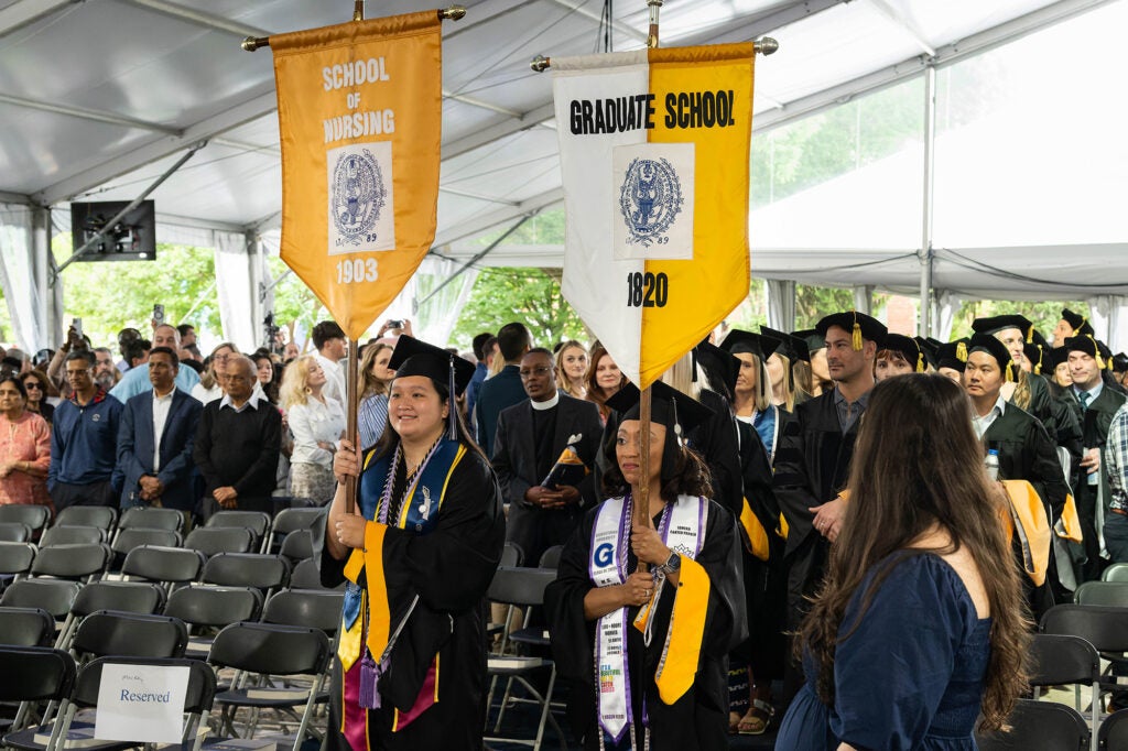 Students process into Commencement proceeded by banners for the school