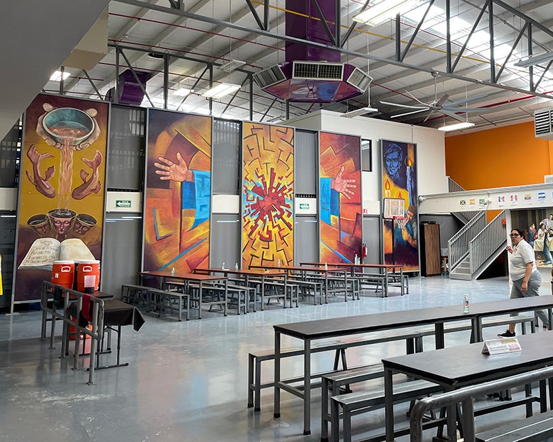 A large institutional interior space set with tables and arrayed with colorful  murals