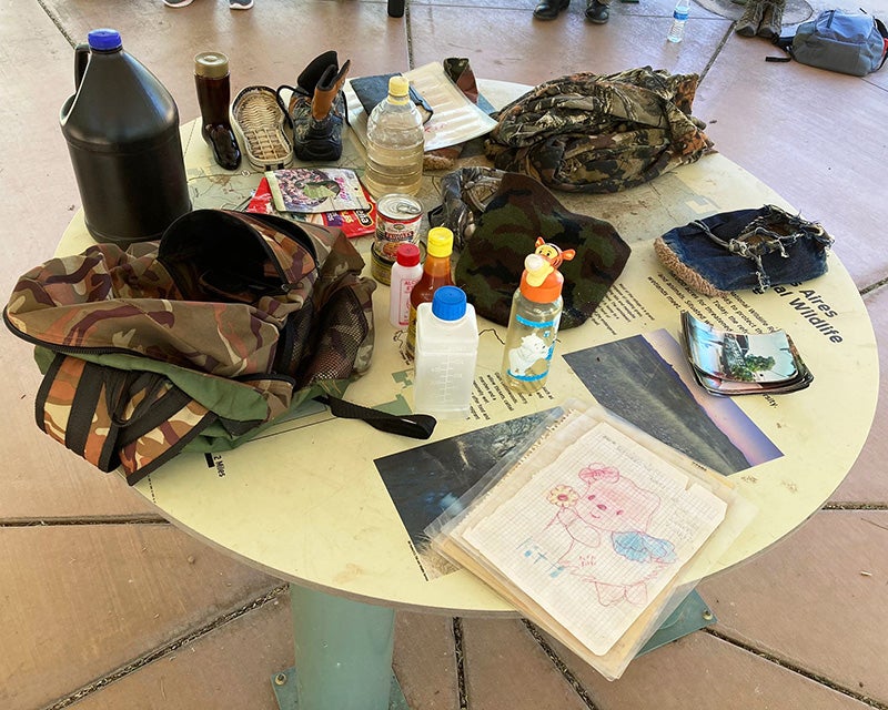 A table arrayed with various belongings including a backpack, bottles and shoes