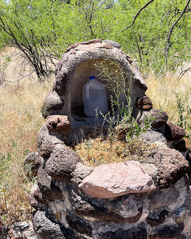 A stone cairn structure holds a plastic water jug