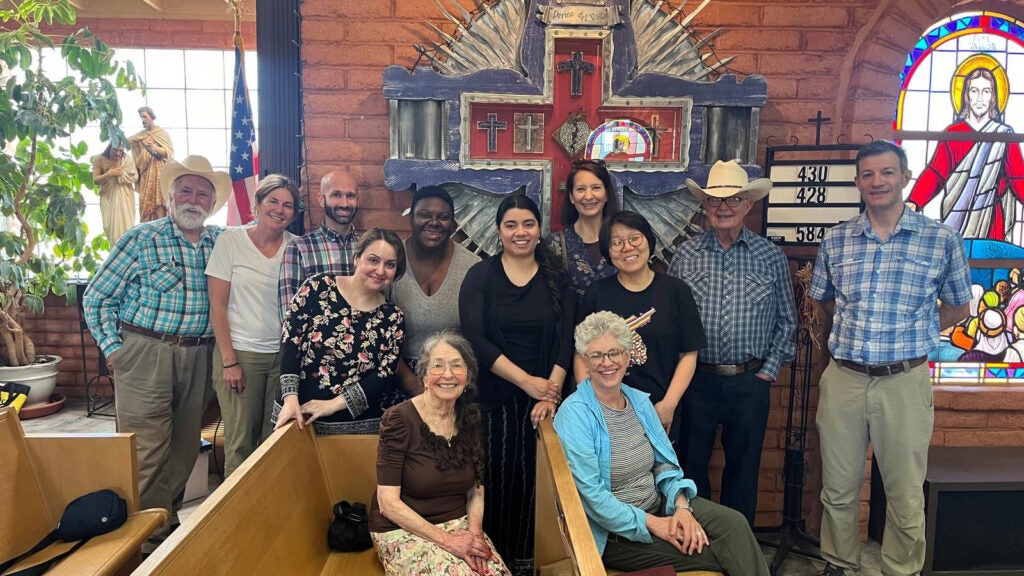 A group of people stand and sit together alongside and in pews inside a church