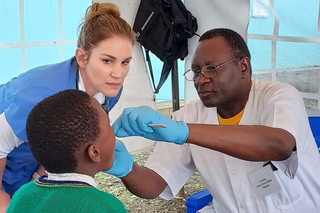 A student looks on as a dentist examines the teeth of a young boy