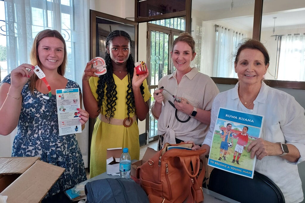 The three students with their instructor, holding a prop from their presentation