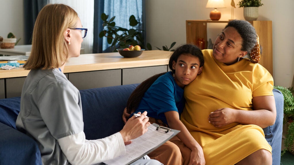 A nurse holding a clipboard speaks with a mother and her child