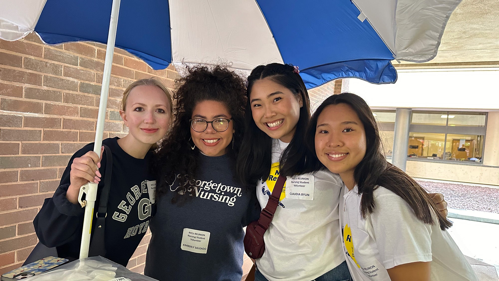 Four student volunteers stand together under an umbrella at the NICU Reunion