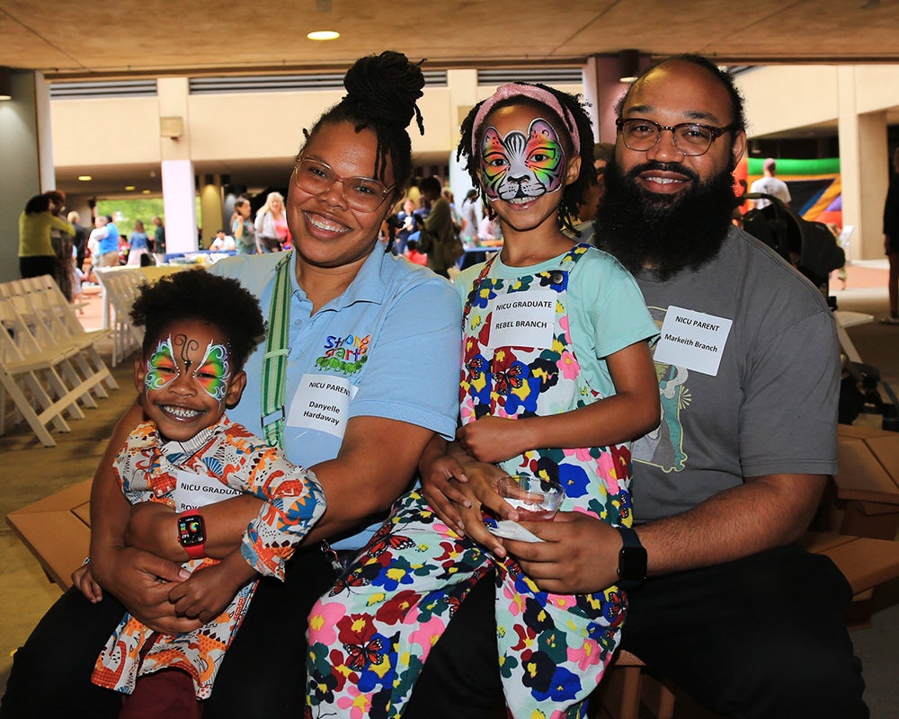 A woman and man hold two small children on their laps who have their faces elaborately painted