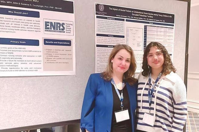 Dr. Alrimawi stands with student Shrishti Chhajlani before two academic papers posted on a wall