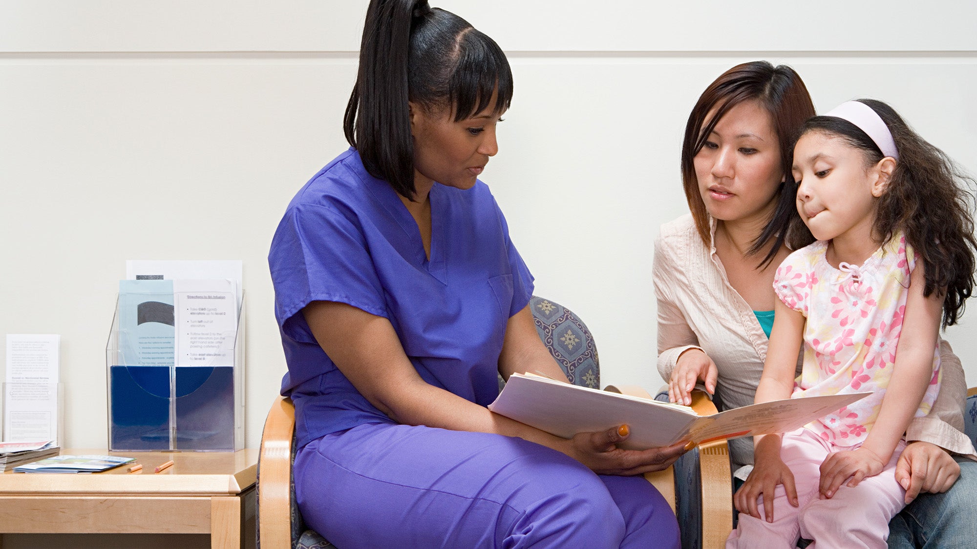 A nurse talks with a mother and child in a doctor's office setting