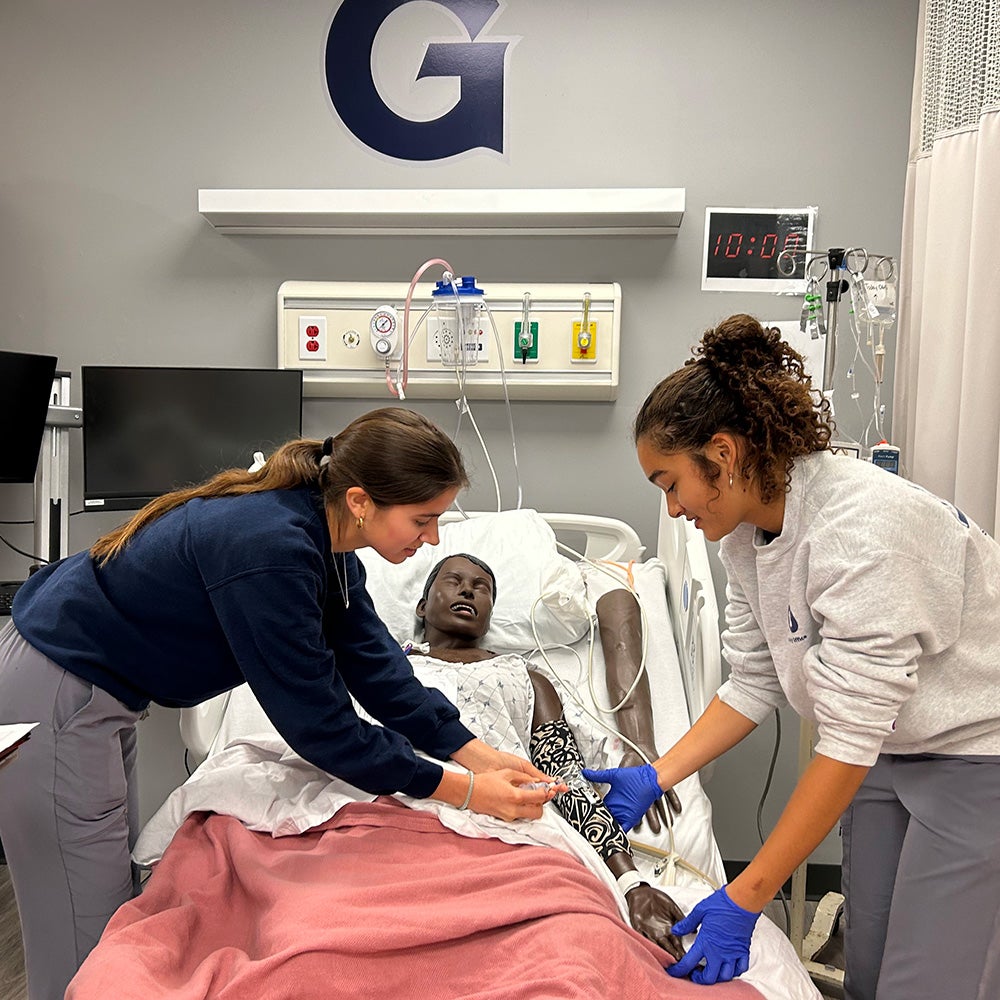 Two students perform a procedure on a simulation dummy in the Sim Lab