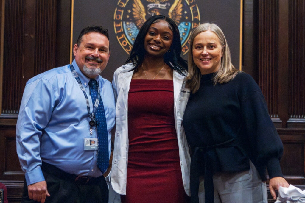 A Black nursing student stands with a male and female faculty member from the school, both of whom are white