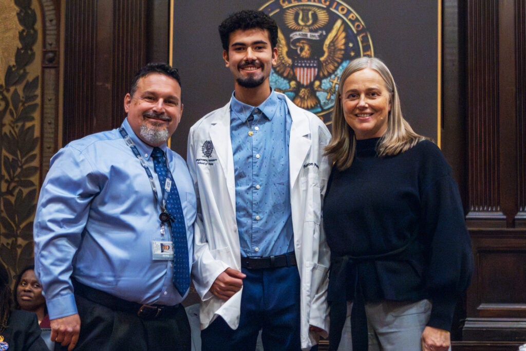 Two nursing faculty members stand together with a nursing student on the stage in Gaston Hall